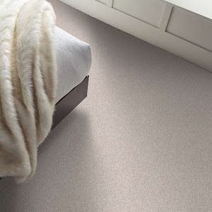 A fluffy blanket on a bed, next to a white cabinet, sits on neutral-colored carpet.