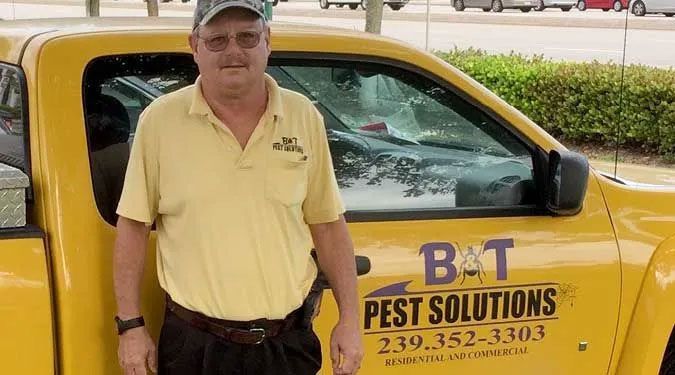 A man is standing in front of a yellow pest solutions truck.