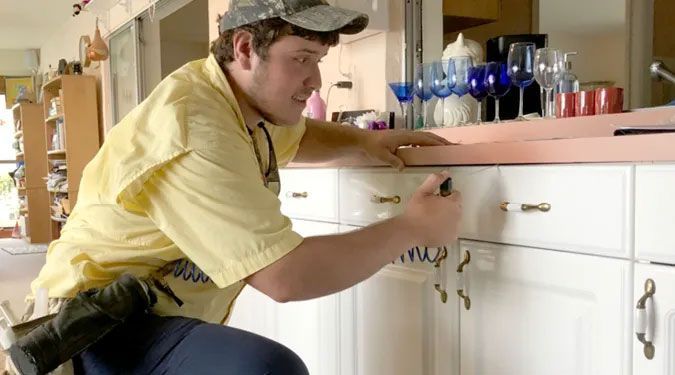 A man in a yellow shirt is working on a kitchen counter.
