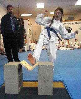 A girl in a martial arts uniform is balancing on two blocks.