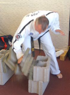 A man in a karate uniform is breaking a concrete block.