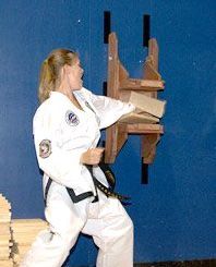 A woman in a karate uniform is standing next to a wooden shelf.