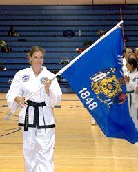 A woman in a karate uniform is holding a blue flag.