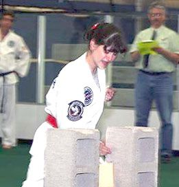 A woman in a white karate uniform is standing next to a brick wall.