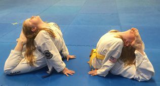 Two young girls are doing stretching exercises on a blue mat.