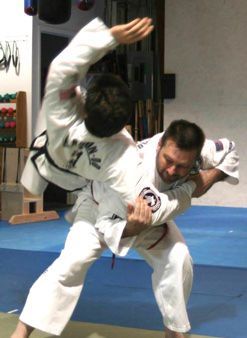 Two men in white karate uniforms are fighting on a blue mat.