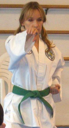 A woman is wearing a white karate uniform and a green belt.