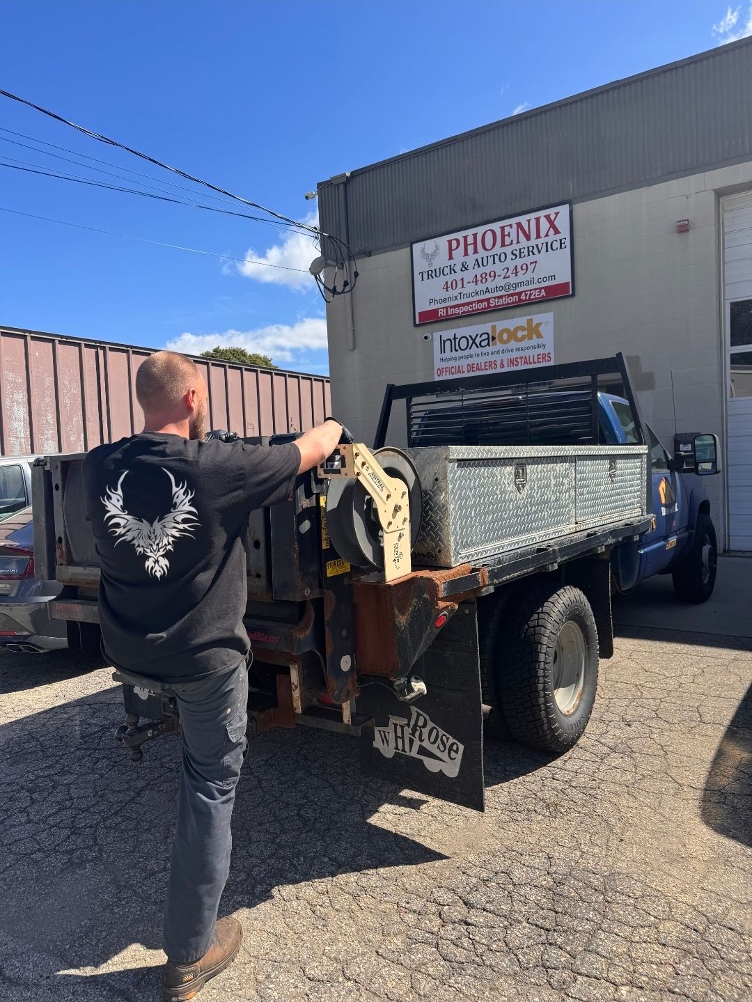Person unloading a metal toolbox from a blue truck beside a warehouse