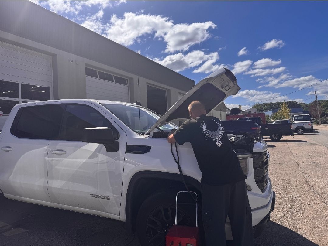 Person loading an upright object into a white pickup truck outside a building on a sunny day
