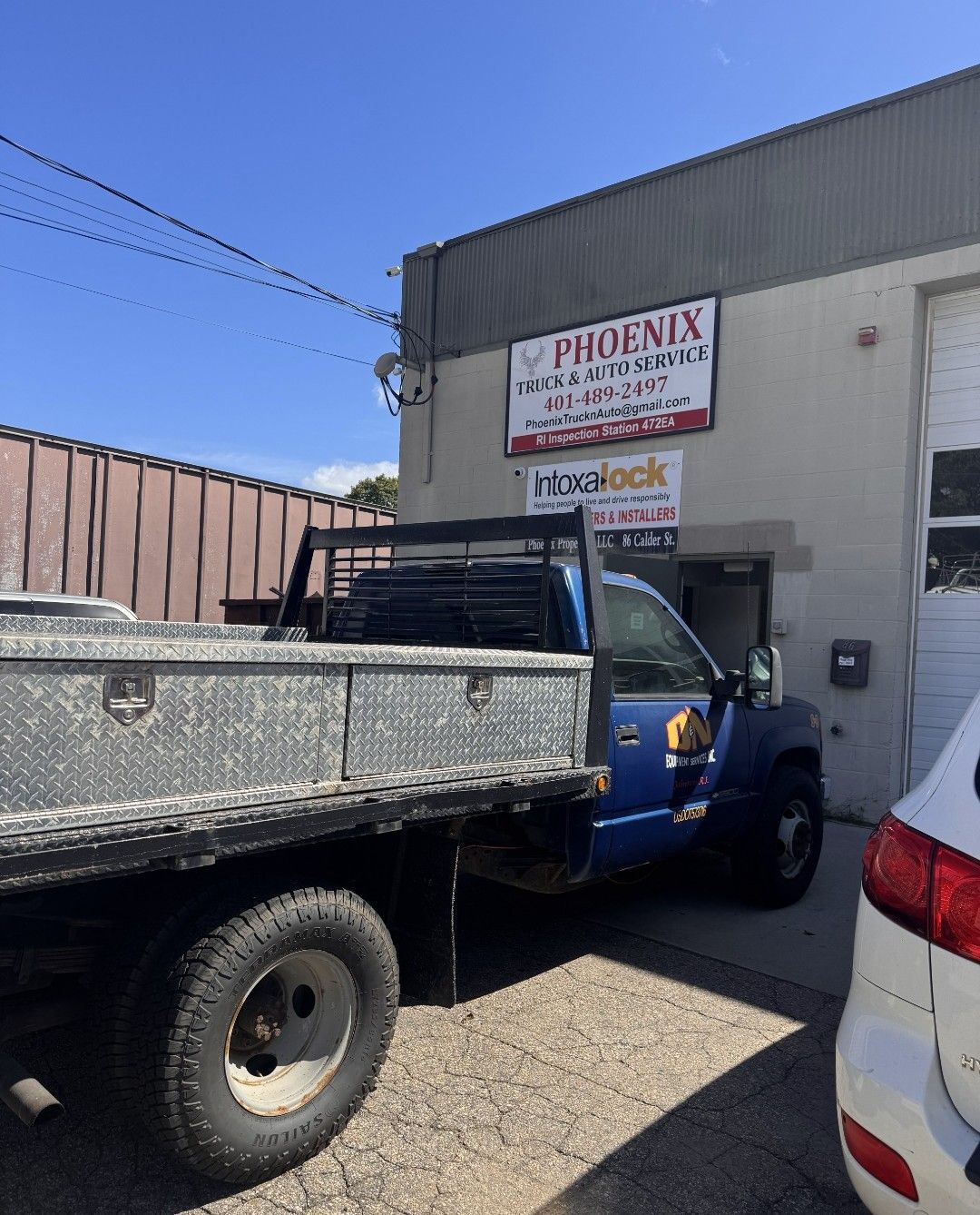Pickup truck parked outside a shop with a sign above the entrance on a sunny day.