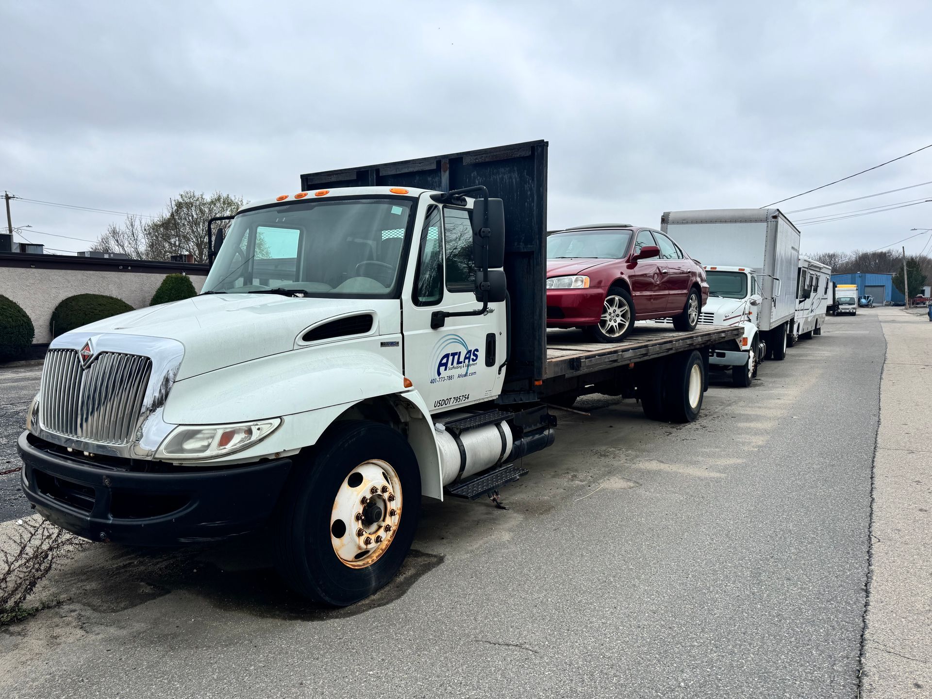 Tow truck hauling a red car on a flatbed along a roadside, with a white truck in front.