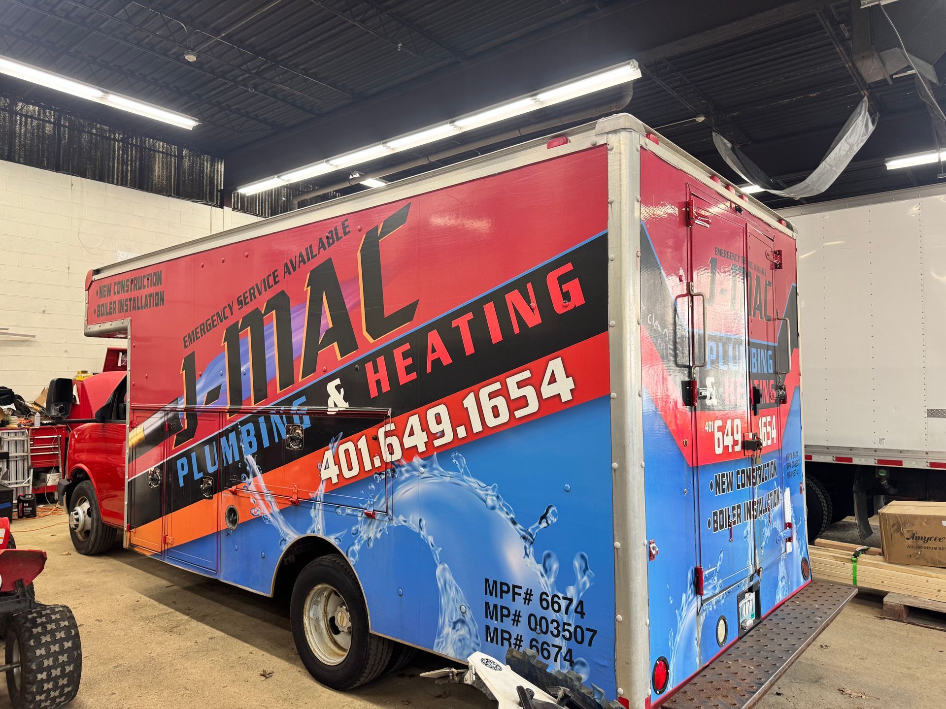 Blue and red plumbing and heating service truck with large “Merival” lettering inside a garage