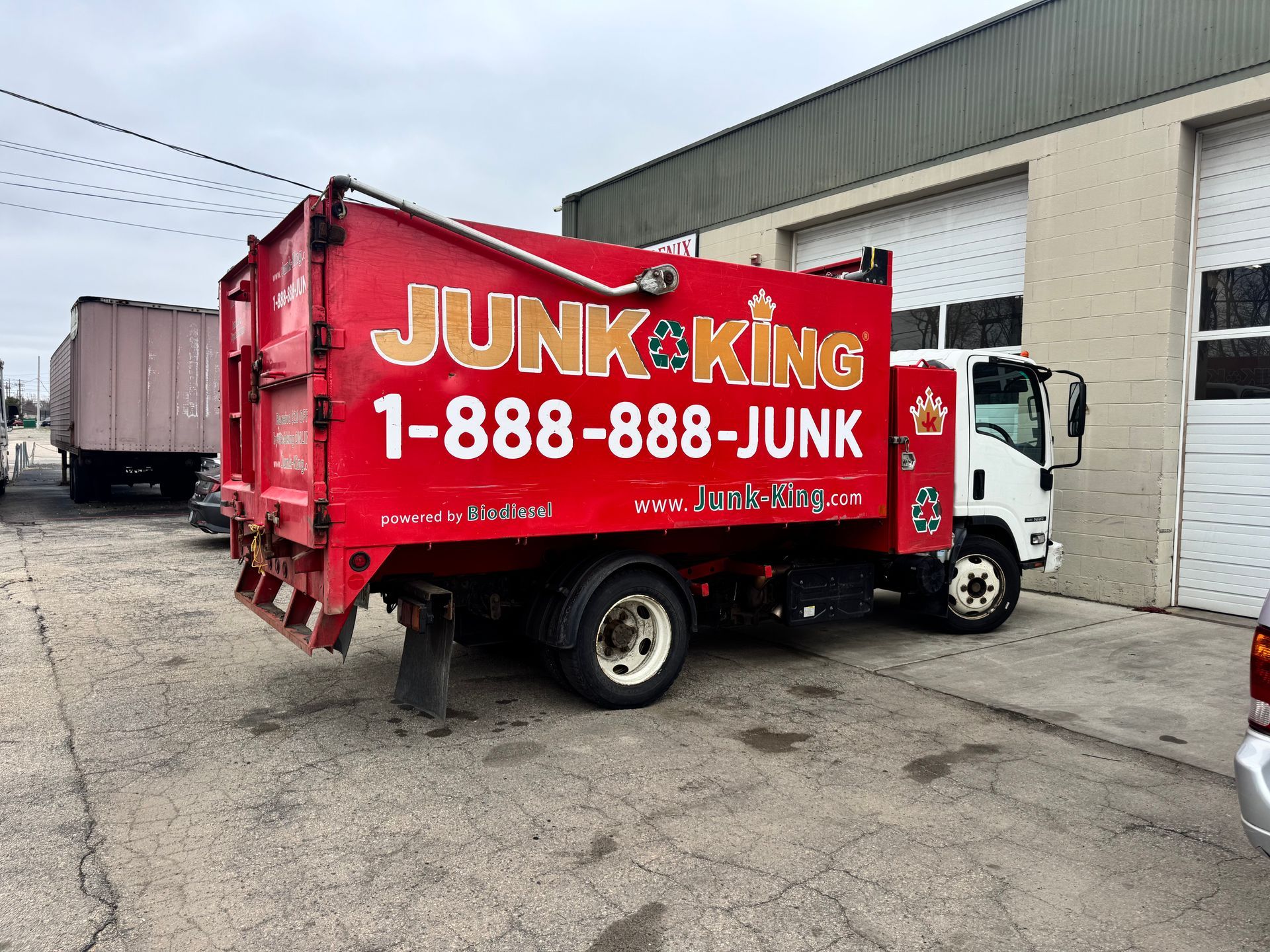 Red Junk King dumpster truck parked in an industrial lot beside a warehouse