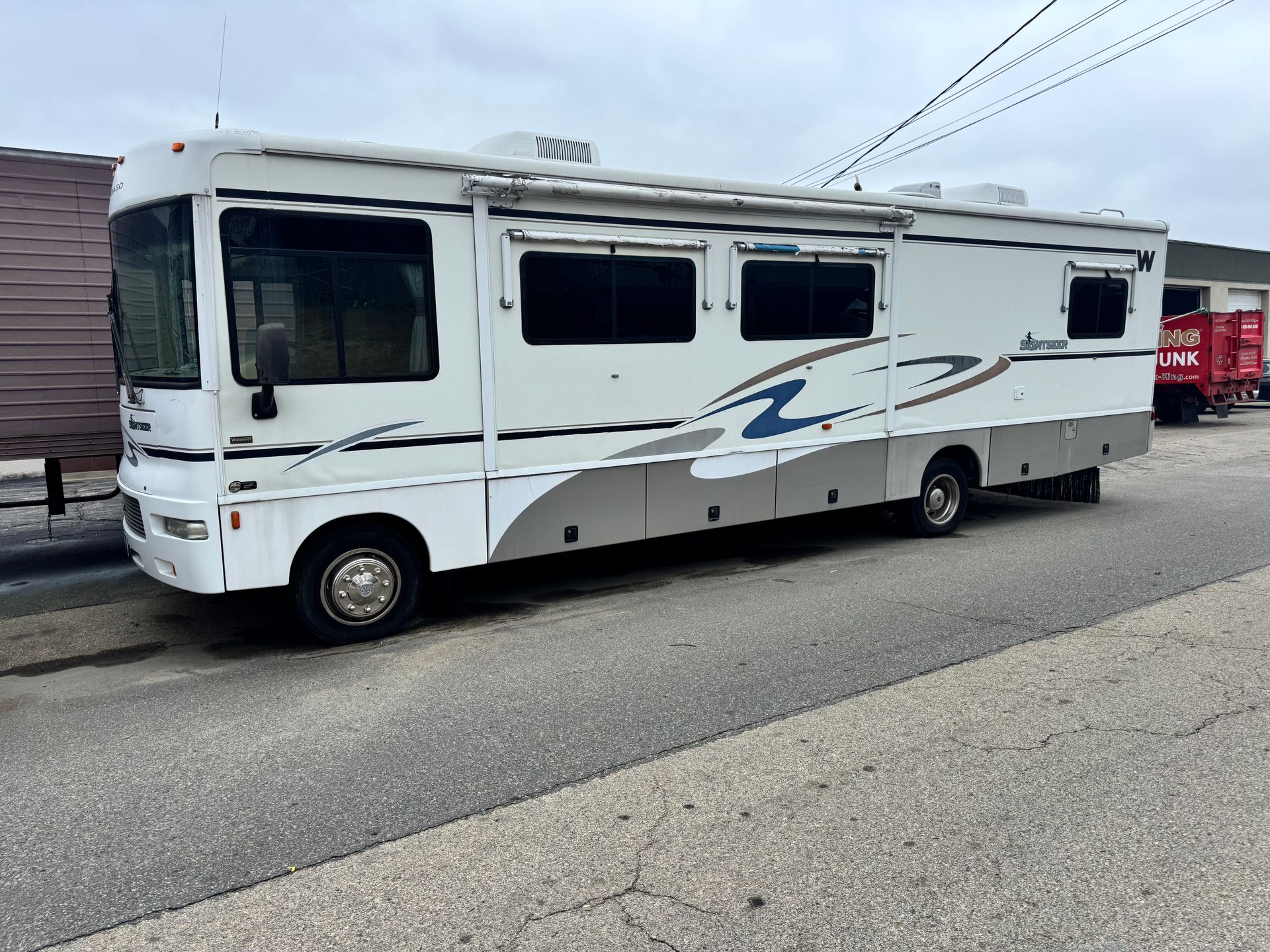 White RV motorhome parked in a lot, side view, with gray and blue graphics