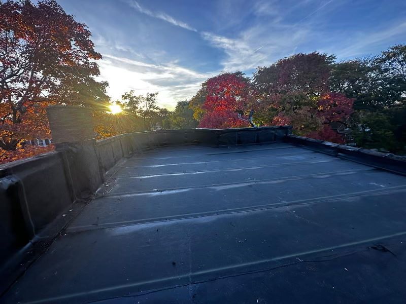 Black rooftop with colorful fall trees under a partly cloudy sky at sunset.