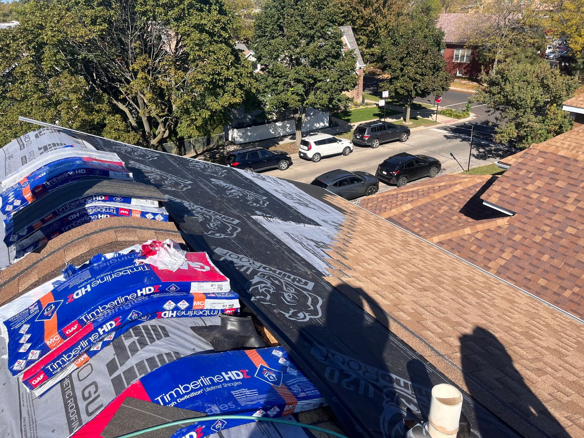 Roof partially covered with shingles and underlayment; street and cars in the background.