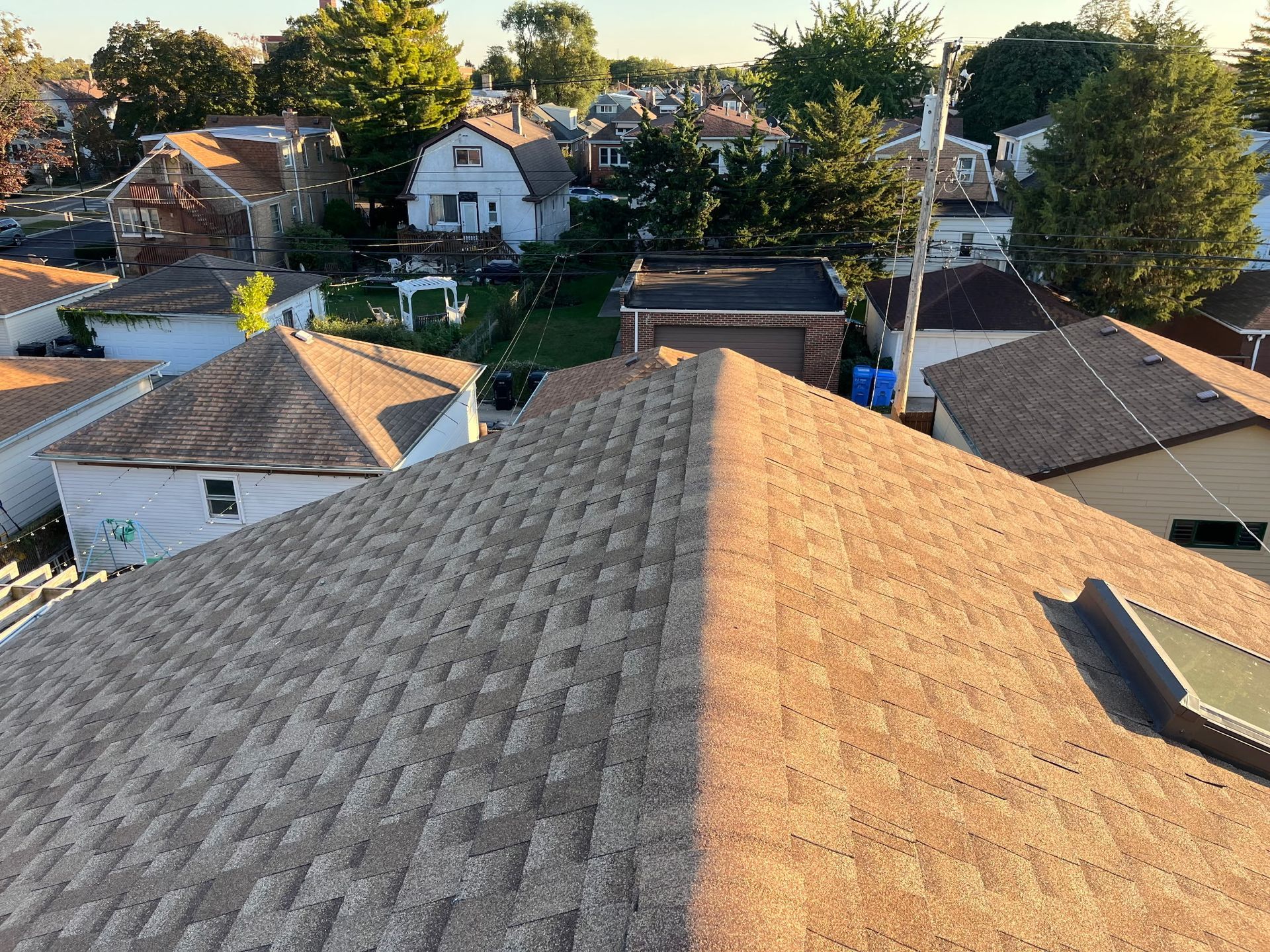 Overhead view of rooftops in a residential area; asphalt shingles in shades of brown and tan.
