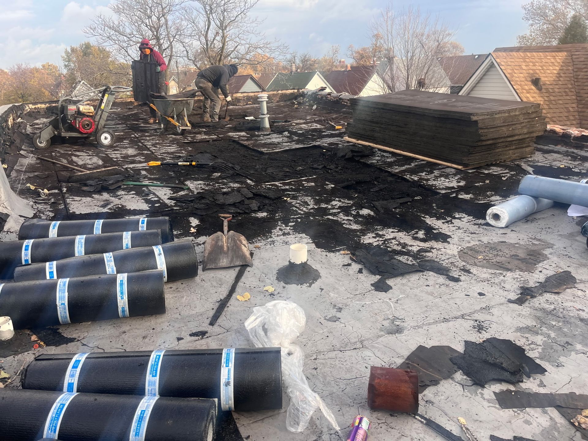 Roofers working on a flat roof, surrounded by roofing materials and equipment.