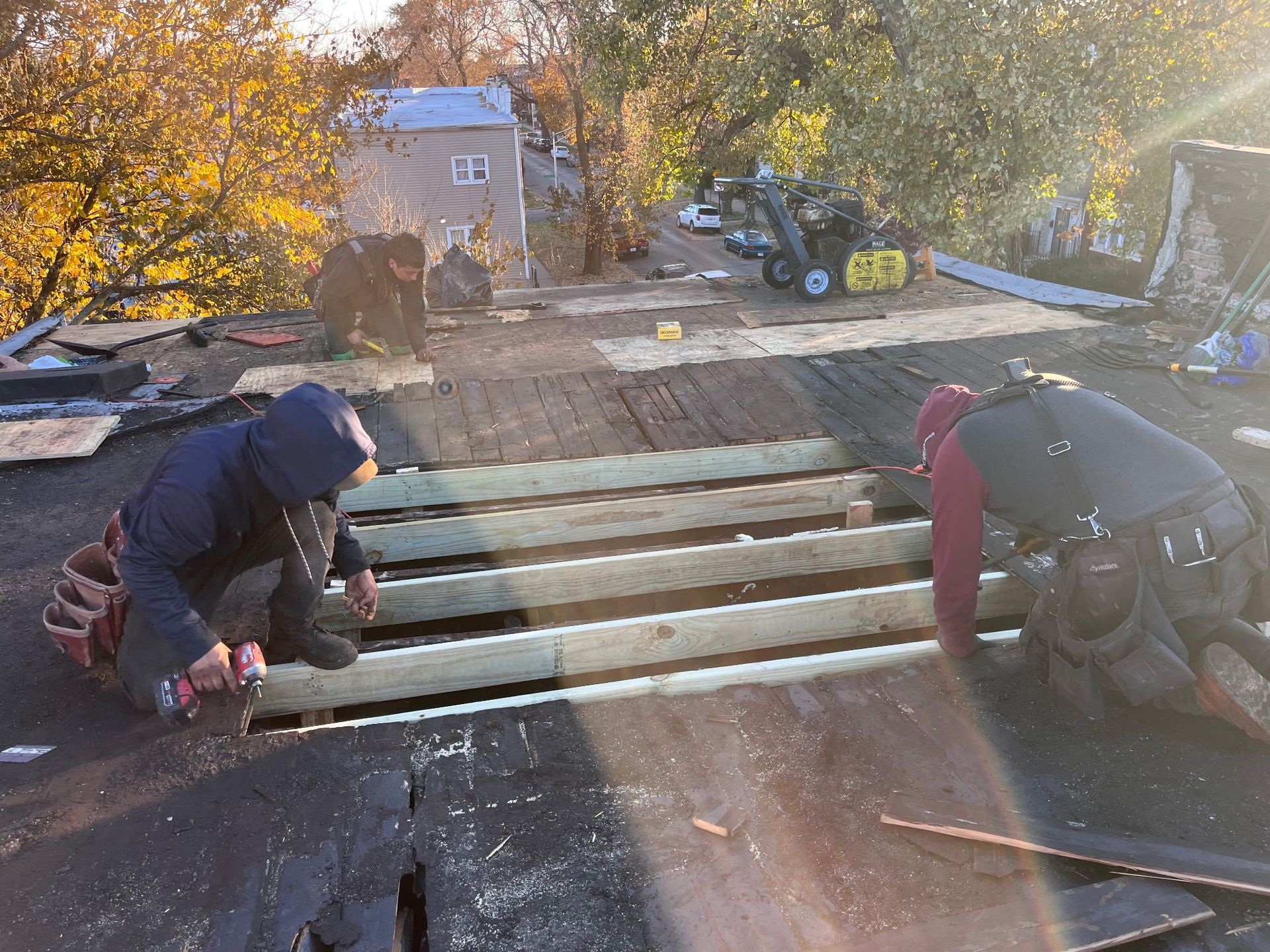 Two roofers repairing a roof, with exposed wooden beams, on a sunny day.