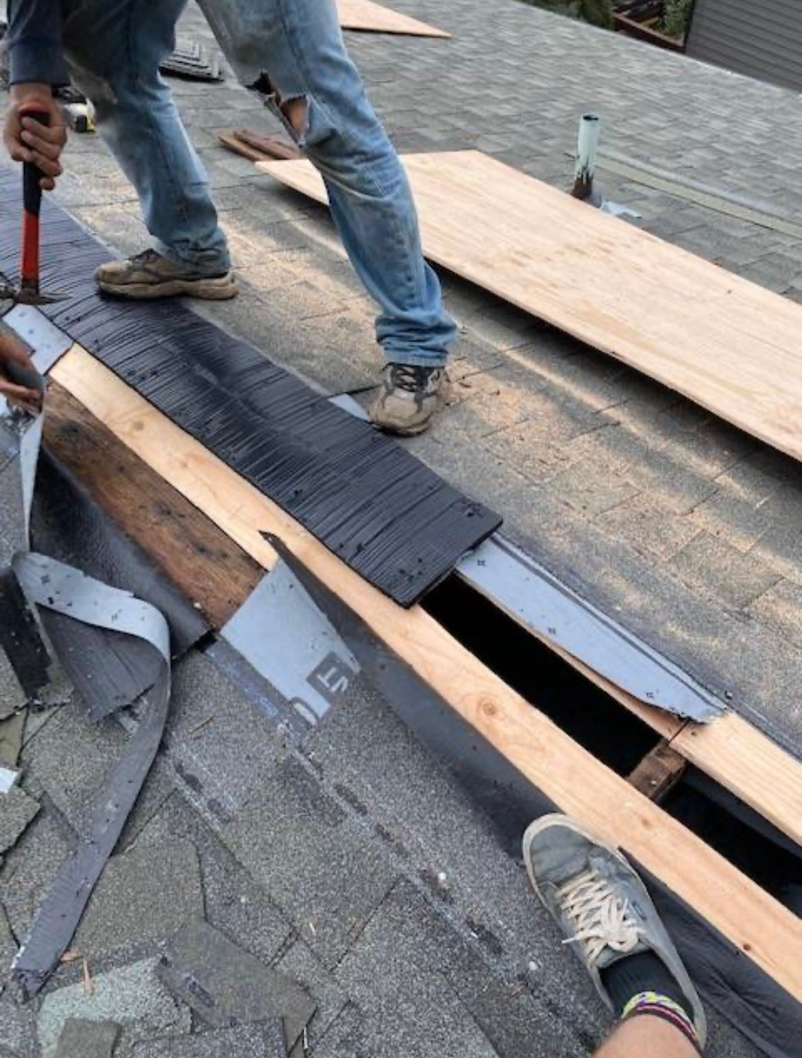 Person on a roof using a hammer, working on a construction project, likely roofing.