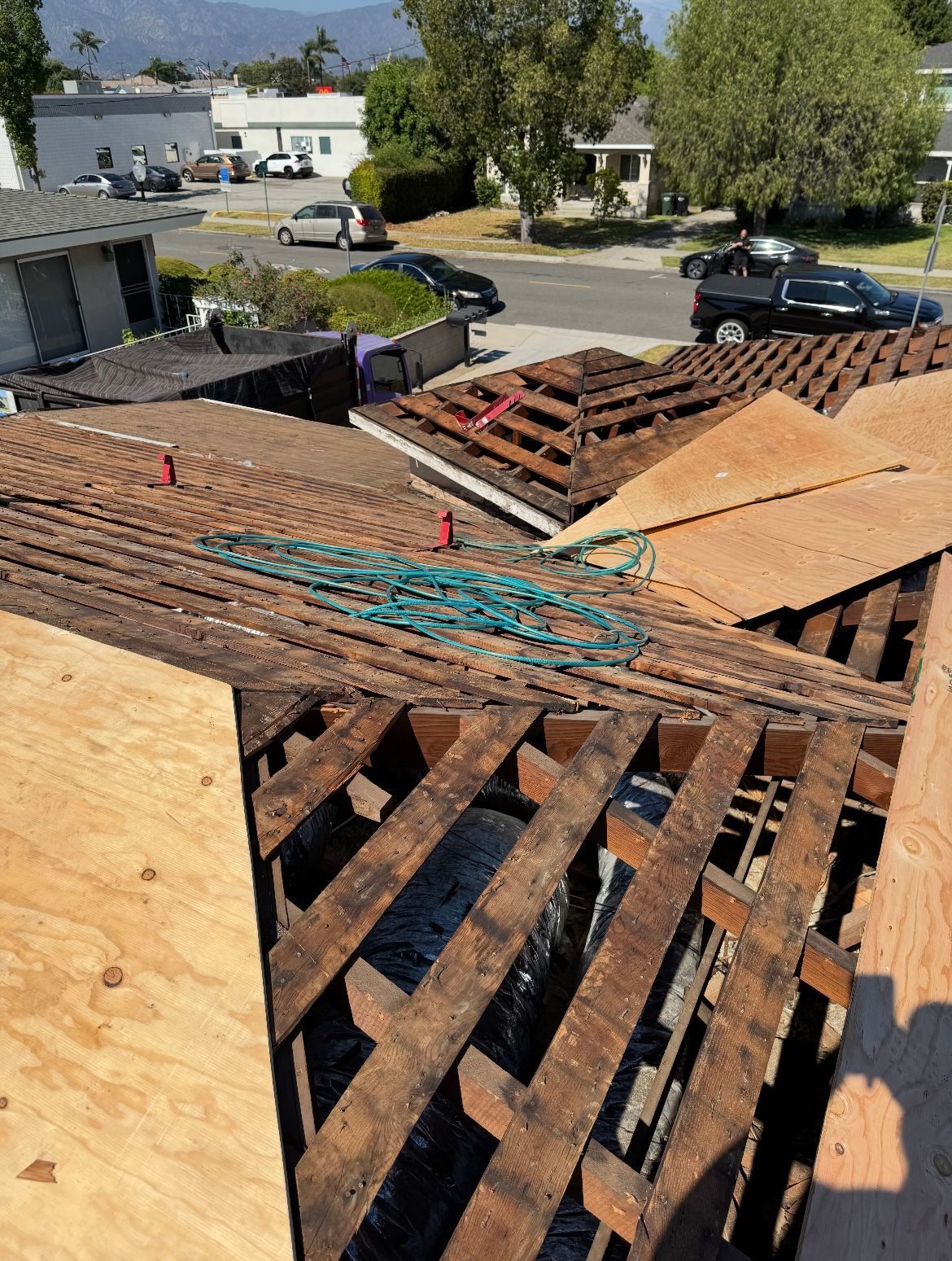 Roof under construction; exposed wooden beams and plywood, partially covered. Green hose on roof.