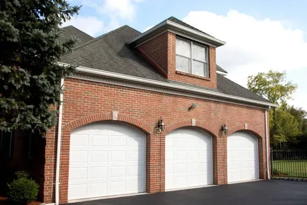 A three-car brick garage with arched white doors and a dormer window under a dark shingled roof.