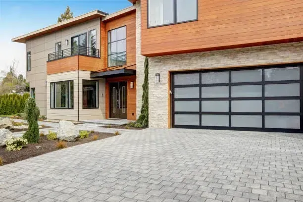 A modern two-story home with wood siding, stone accents, a multi-pane frosted glass garage door, and a paved driveway.