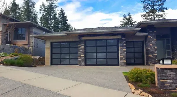 A modern suburban house with a three-car garage featuring black-framed glass panel doors and stone exterior accents.