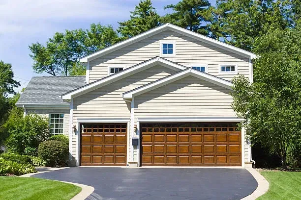 A two-story suburban house with beige siding, a gray roof, and a three-car garage featuring brown wooden doors.