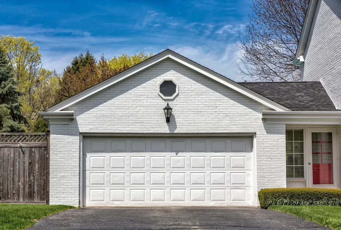 White brick garage with a paneled door, a central light, and a small octagonal window, set beneath a bright blue sky.