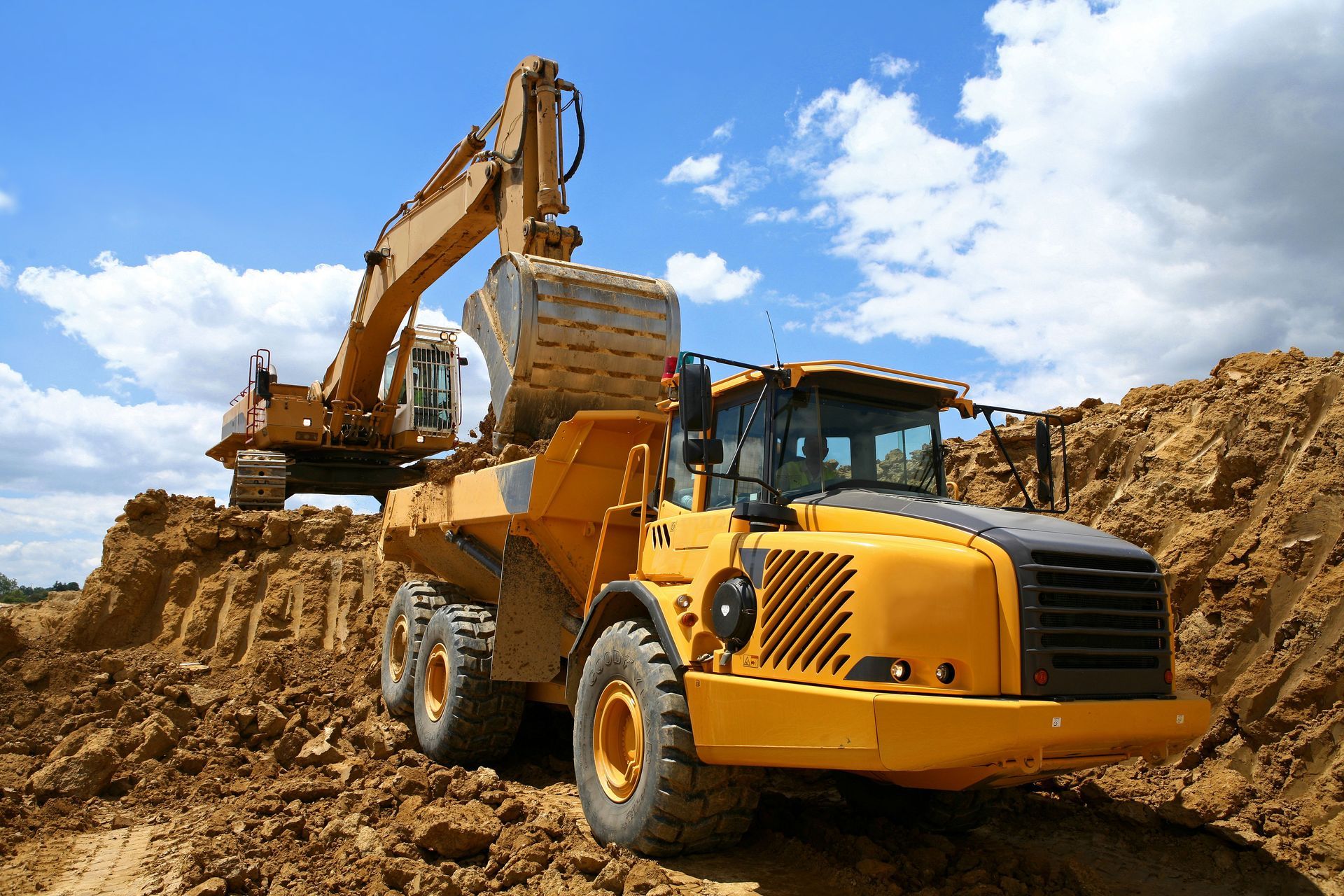 A dump truck is being loaded with dirt by an excavator.