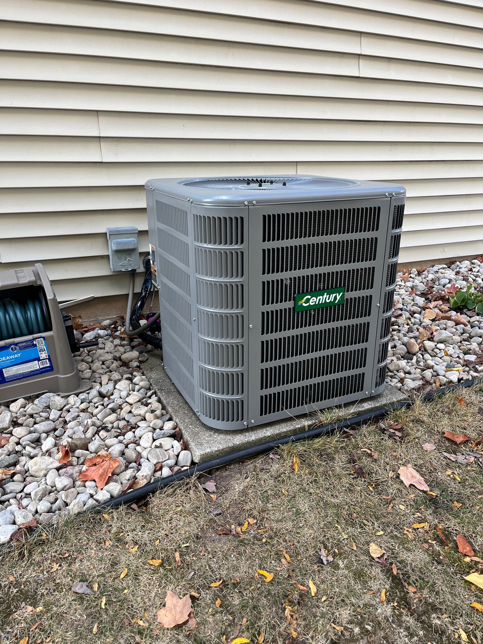 A gray air conditioner is sitting on the side of a house.