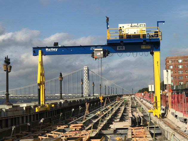Yellow bridge maintenance crane over a suspension bridge deck with cables in the background