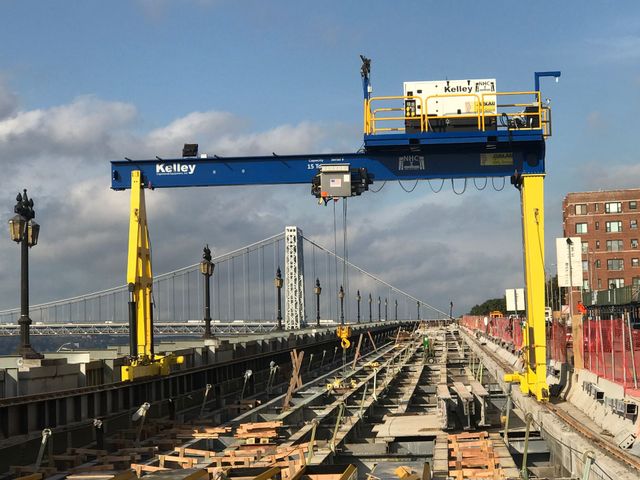 Yellow bridge maintenance crane over a suspension bridge deck with cables in the background