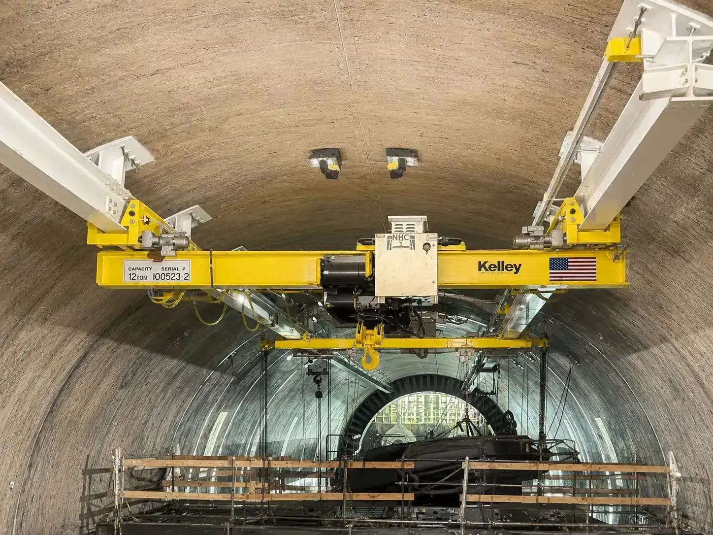 Yellow maintenance machine inside a tunnel, with a hanging work platform below an arched concrete ceiling.