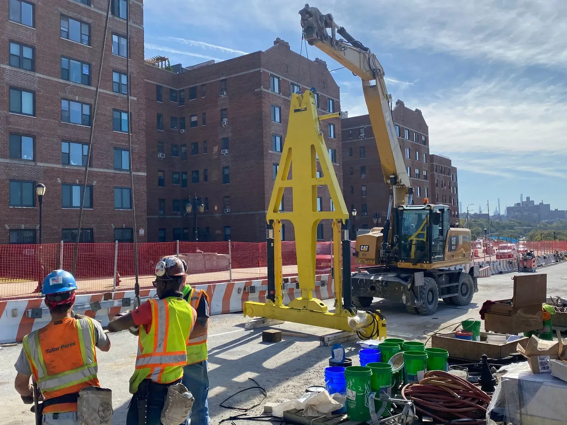 Construction workers beside a crane lifting a yellow steel frame on a city street.