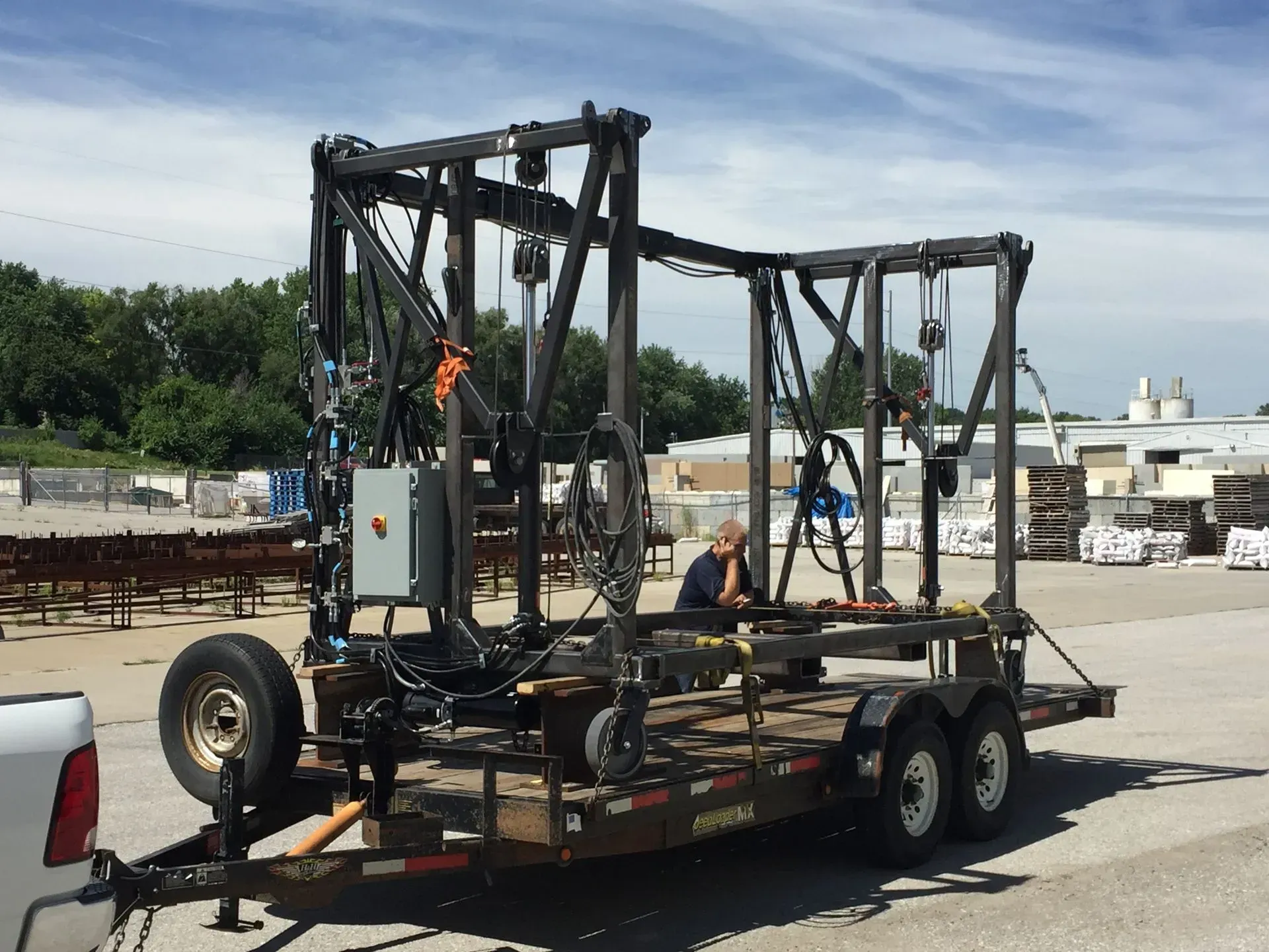 Flatbed trailer carrying a large black metal frame in an outdoor industrial yard.
