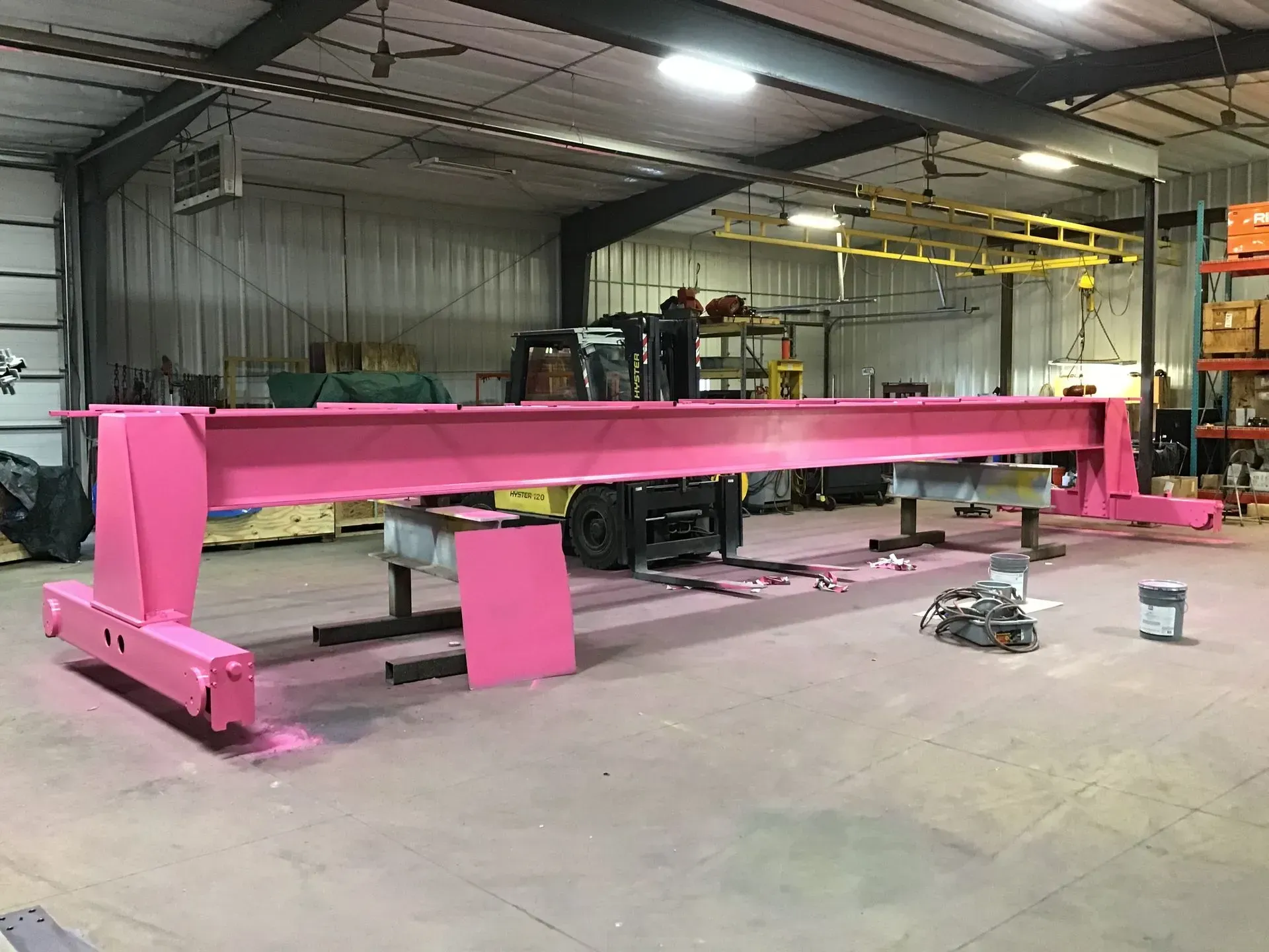 Bright pink industrial steel beam in a warehouse workshop, with machinery and tools around it.
