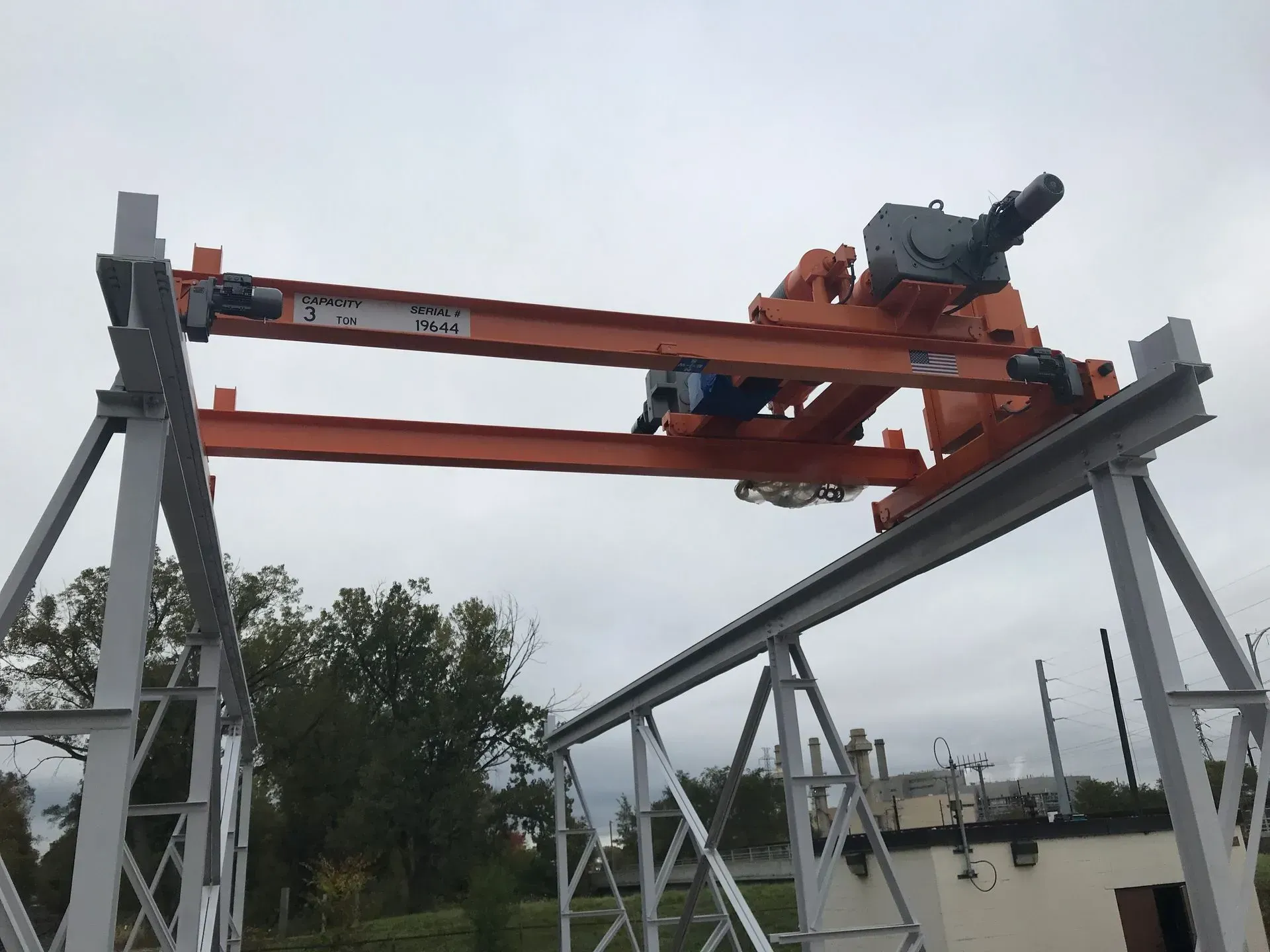 Orange crane on a gray steel frame outdoors against a cloudy sky.