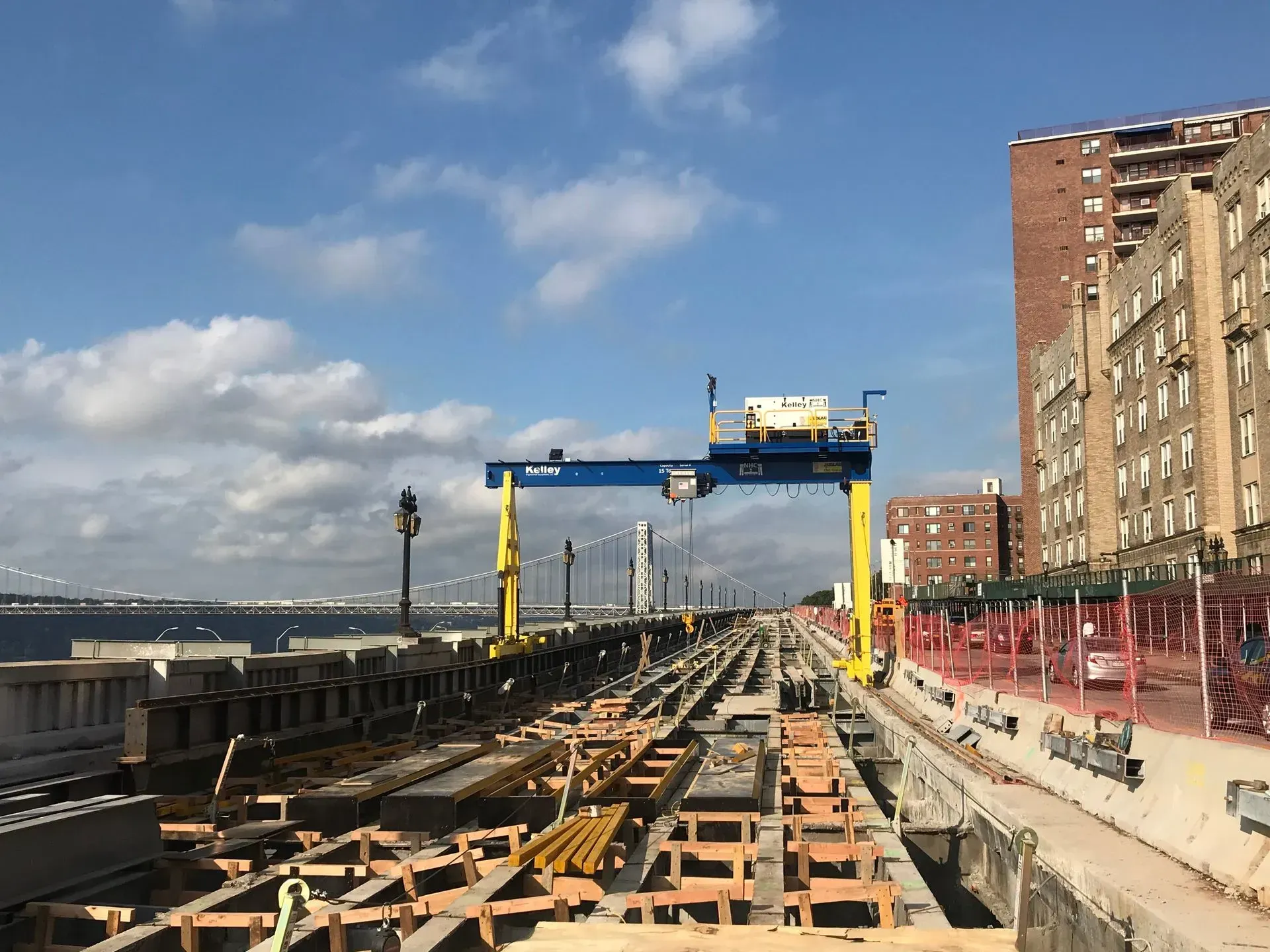 Construction site on a waterfront pier with yellow gantry crane, debris, and buildings under a blue sky.