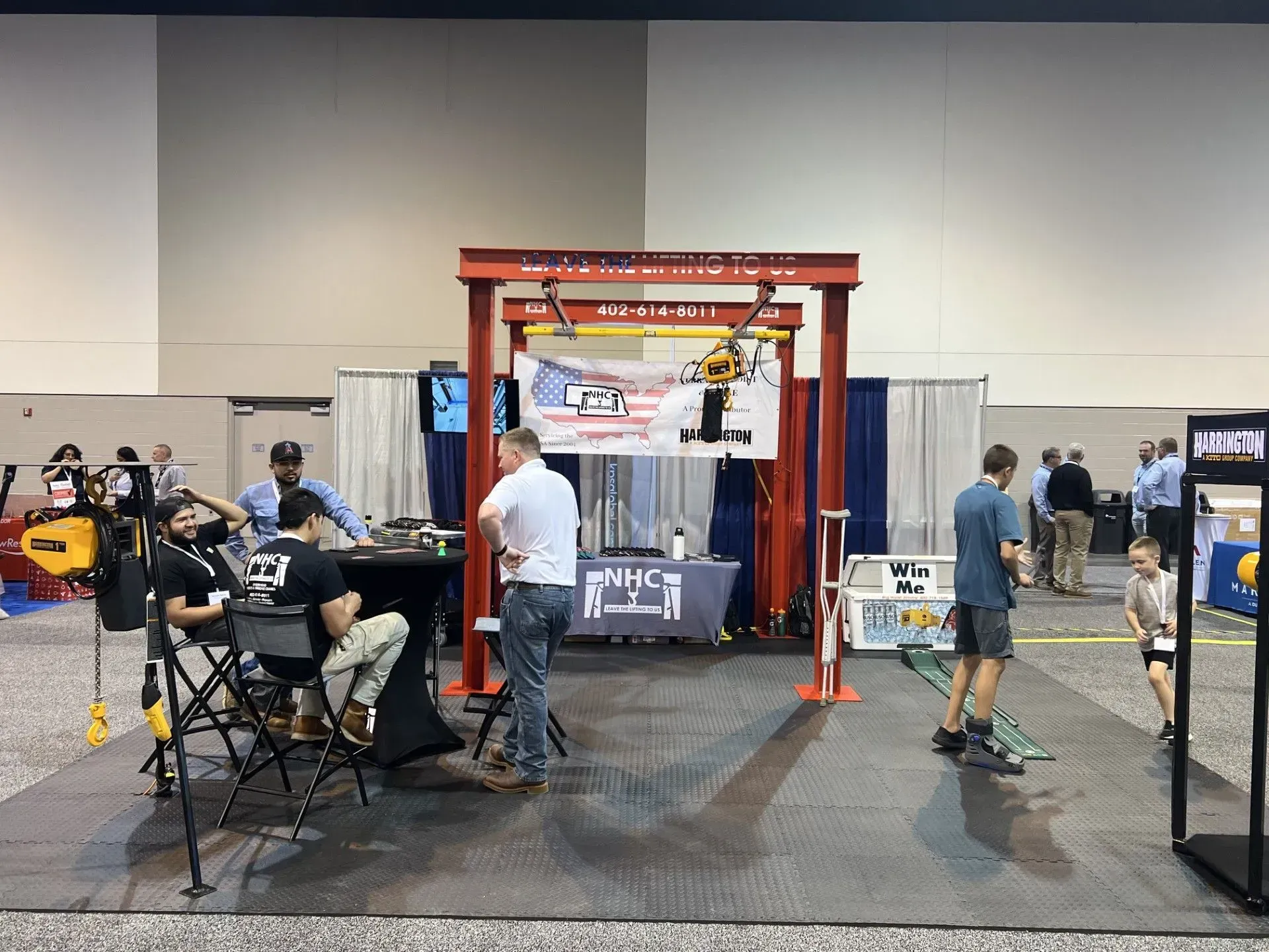 Trade show booth with a red arch, people seated and standing, and a blue curtain backdrop.