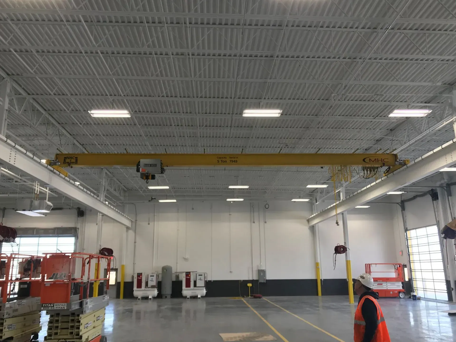 Empty industrial warehouse with a yellow overhead crane and high ceiling lights.