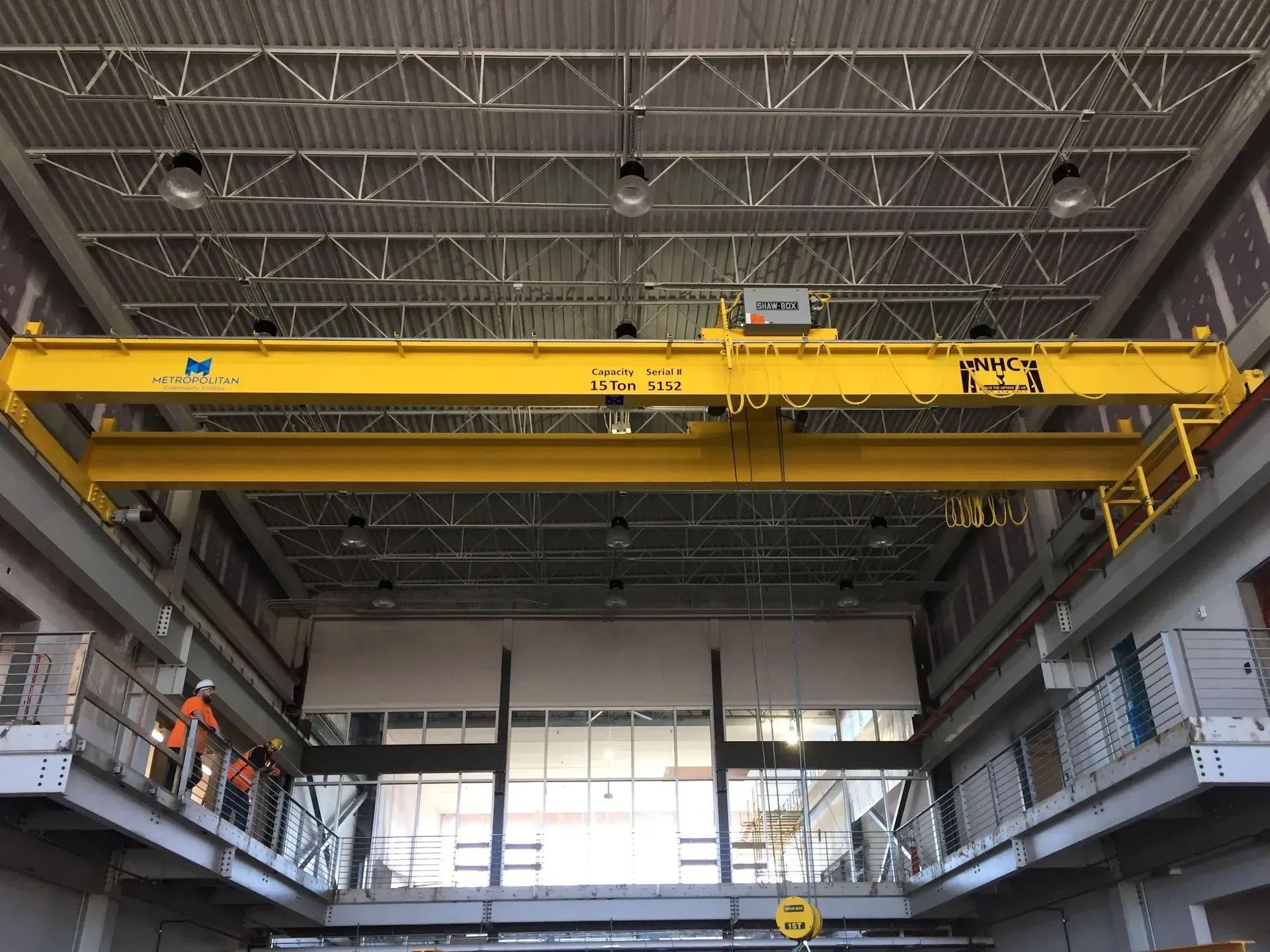 Yellow overhead crane inside an industrial warehouse with high ceiling and catwalks.