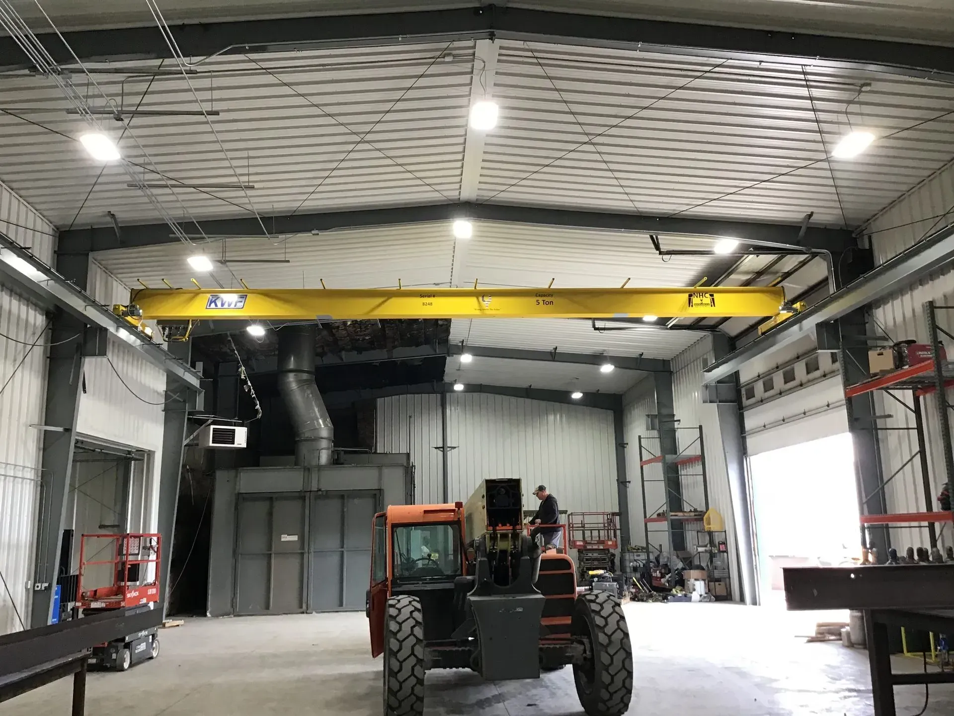 Industrial warehouse interior with a yellow overhead crane, large open doors, and a tractor in the center.