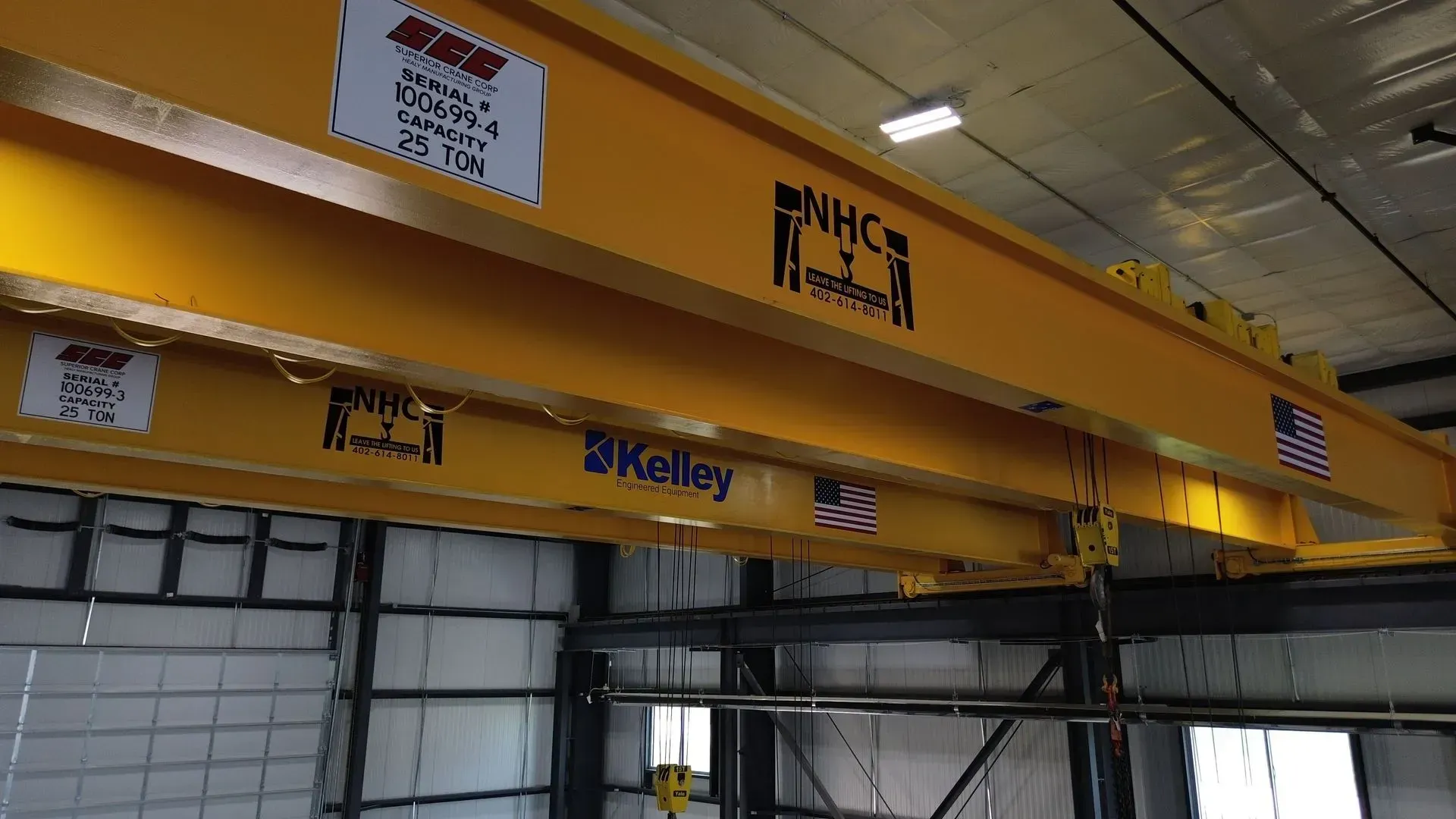 Yellow overhead industrial crane beams in a warehouse with logos and hanging equipment.