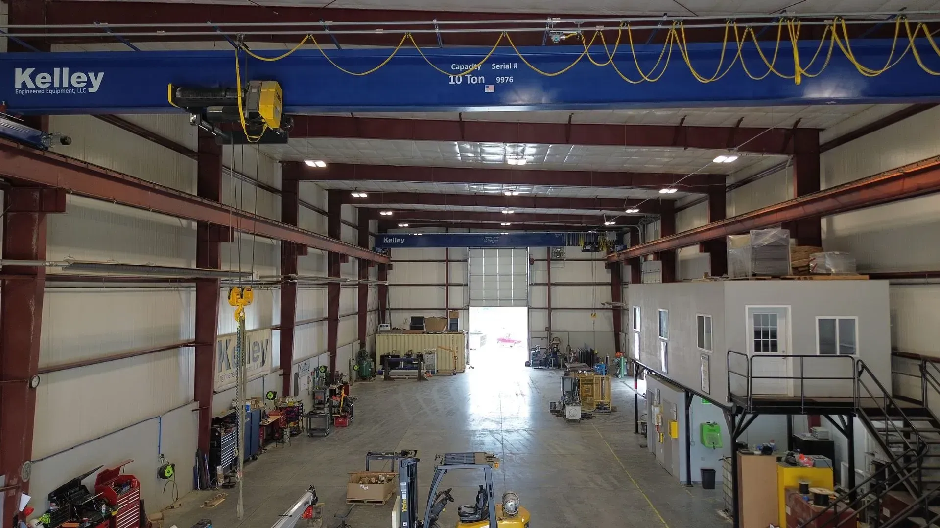 Interior of an industrial warehouse with steel beams, overhead crane rails, and machinery on the floor.
