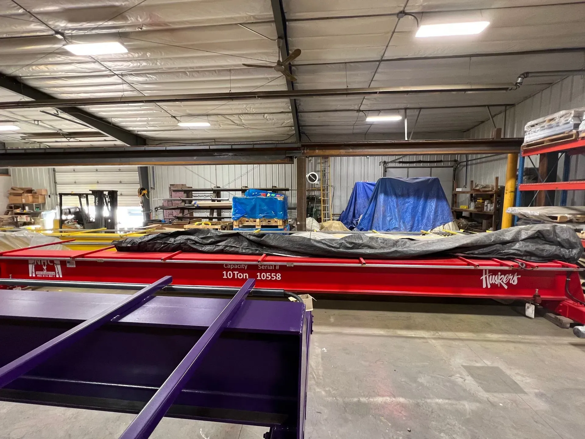 Industrial workshop with a large red machine and purple foreground equipment under blue tarps.