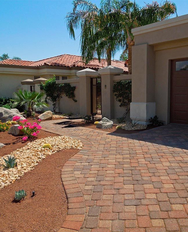 A brick driveway leading to a house with palm trees in the background