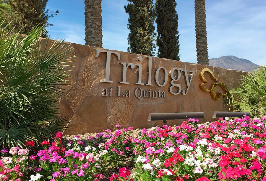 A sign for trilogy at la quinta is surrounded by flowers