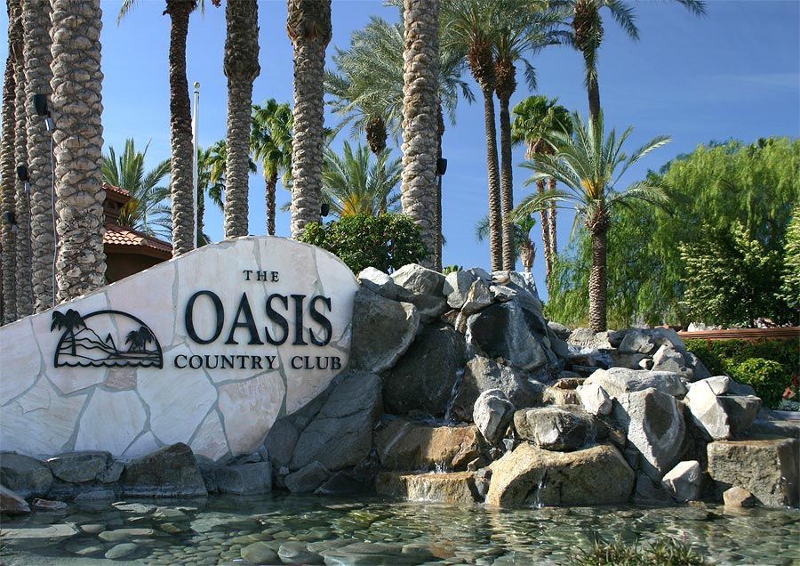 A sign for the oasis country club surrounded by palm trees